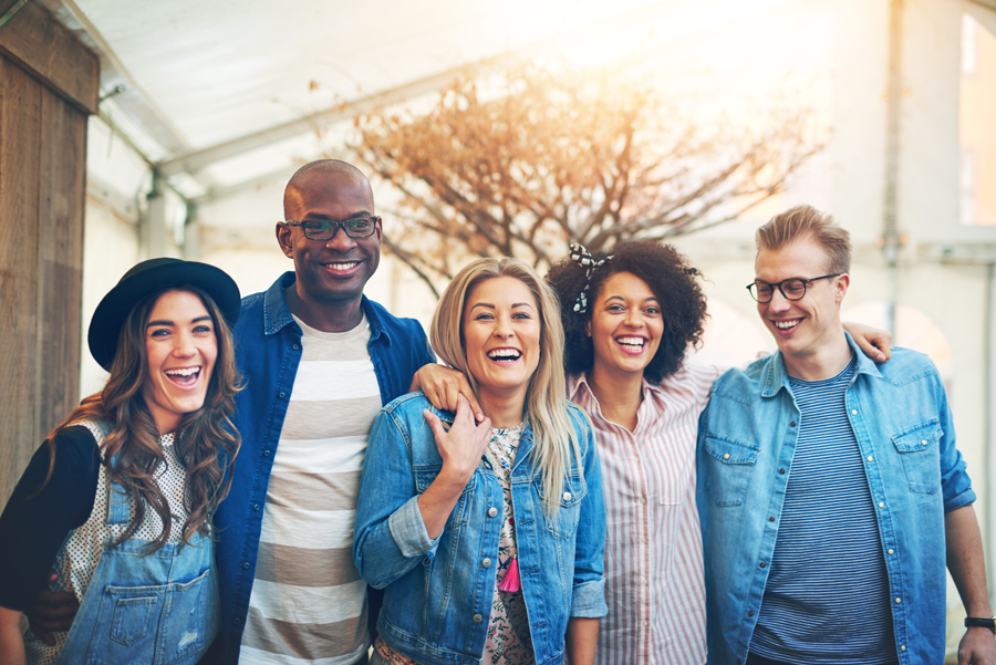 Group of five young people standing closely together, laughing and smiling posing to camera,